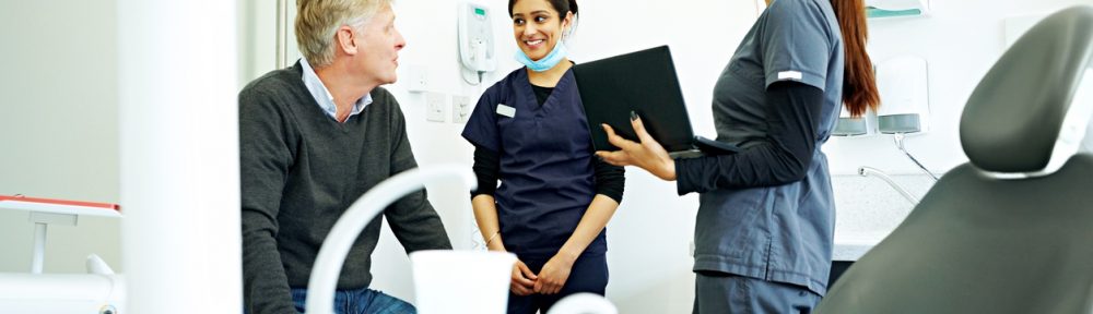 A dentist talks with two staff members in a dental office.