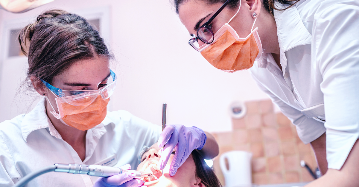 A dental hygienist and dental assistant perform routine oral care on a patient.