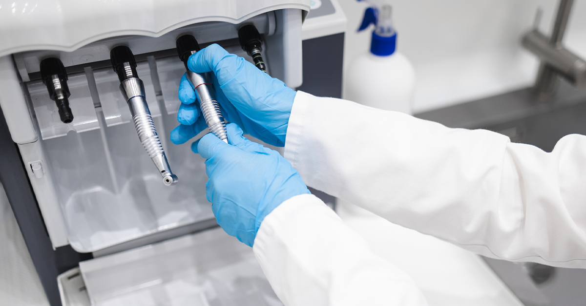 Close up of a dental worker sanitizing and lubricating a dental handpiece.