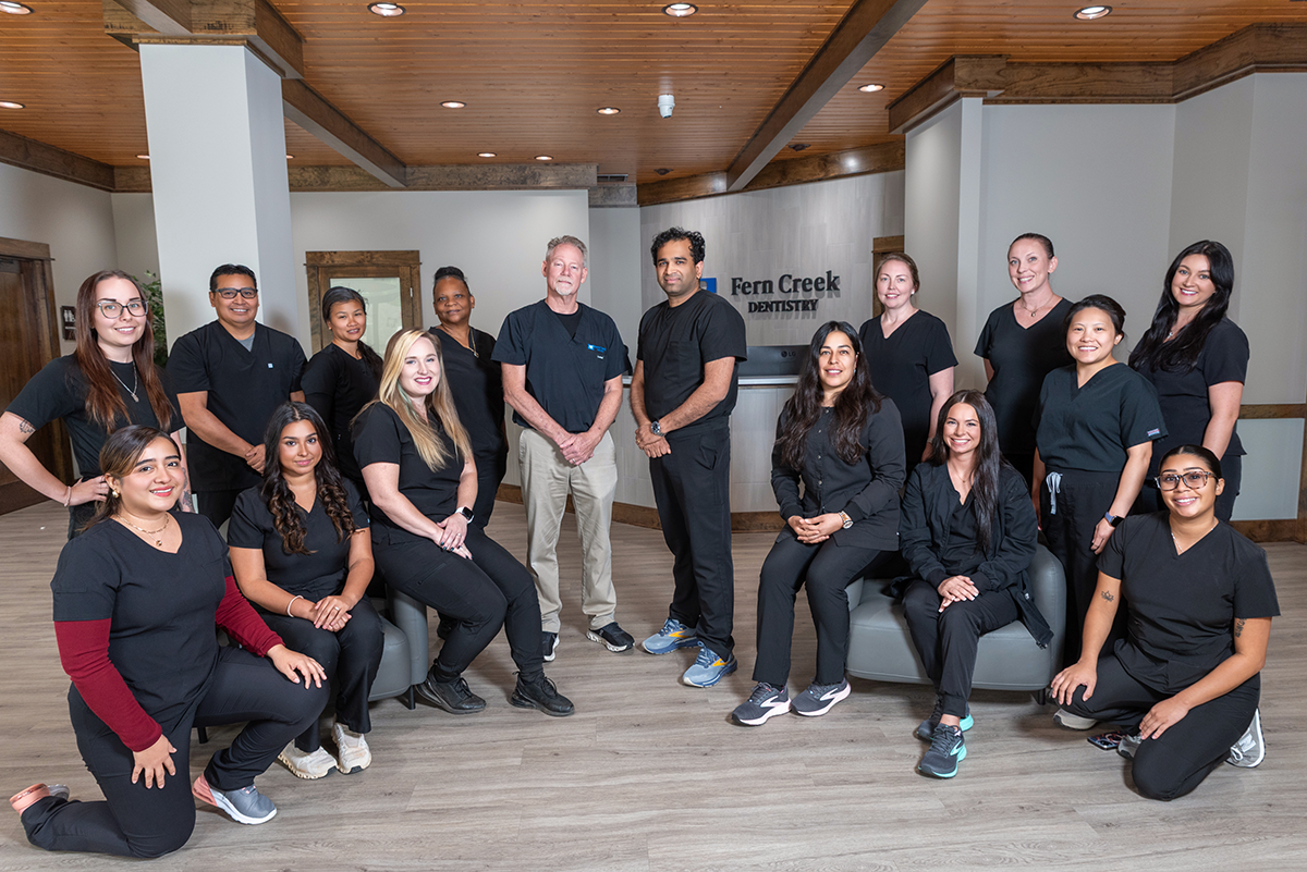 Dental team posing together in the lobby of Fern Creek Dentistry, wearing black scrubs in a modern, wood-accented office.
